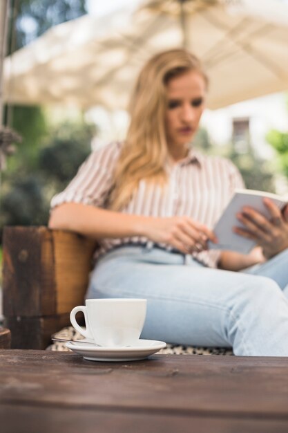 Free photo cup of coffee on table in front of woman reading book