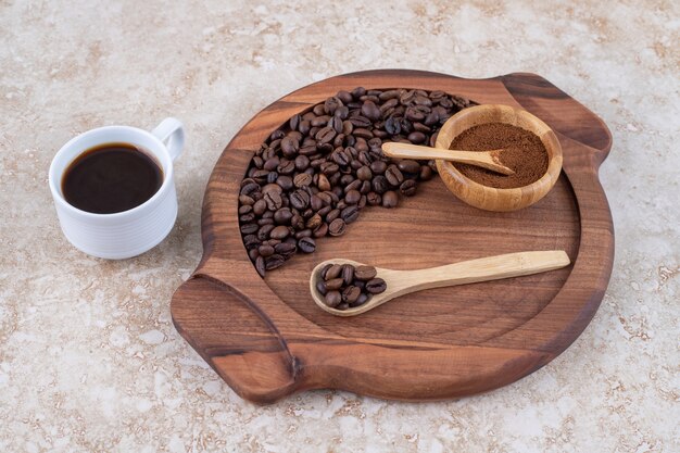 A cup of coffee next to a tray of coffee beans and ground coffee powder 