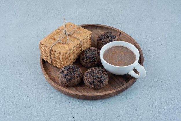 Cup of coffee and various cookies on wooden plate