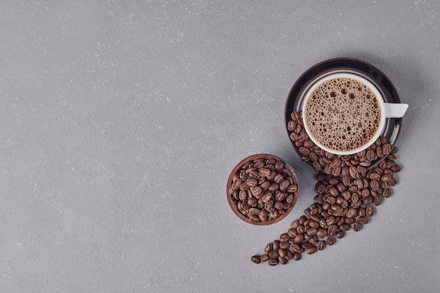 A cup of coffee with arabica beans around, top view.