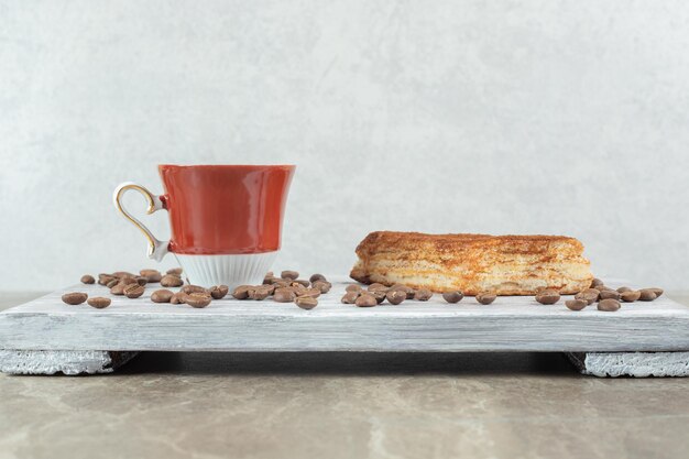 Cup of coffee with beans and pastry on wooden board. 