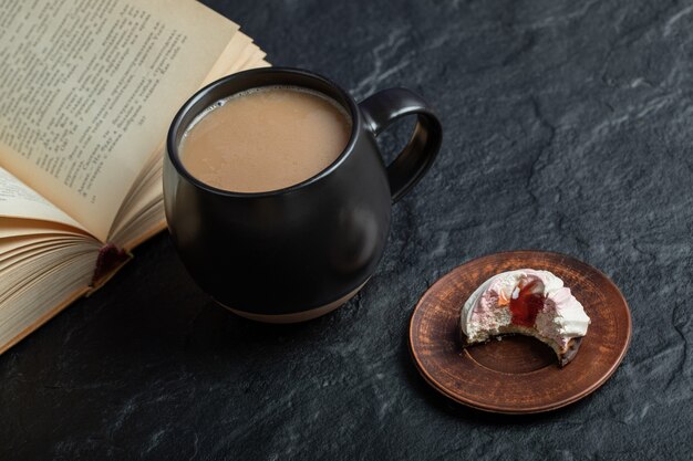 A cup of coffee with book and bitten cupcake. 