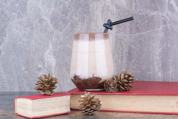 A cup of coffee with book and pinecones on marble.