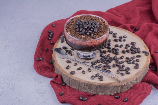 A cup of coffee with chocolate beans on wooden board.