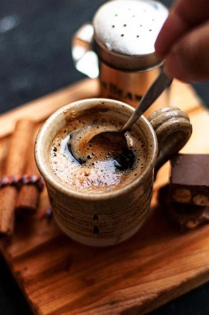 Cup of coffee with cinnamon sticks and chocolate cookies on a wooden board