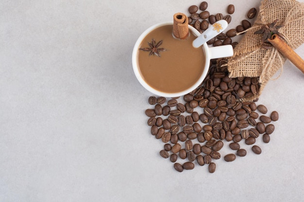 Чашка кофе с палочками корицы и кофейными зернами на мраморном фоне. Фото высокого качества