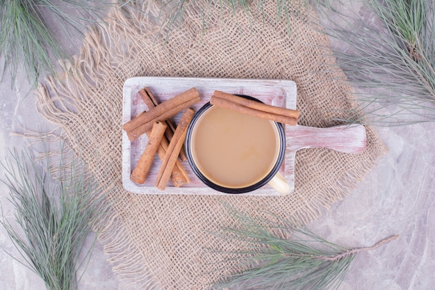 A cup of coffee with cinnamon sticks on rustic wooden board.