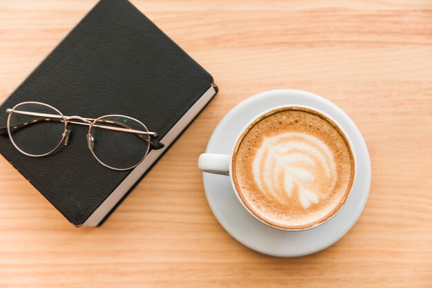 Cup of coffee with diary and spectacles on wooden background