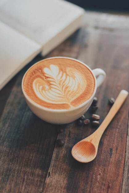 Tazza di caffè con il disegno sulla schiuma e un libro