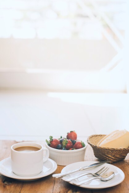 Cup of coffee with fresh berries and cutlery on plate against wooden background