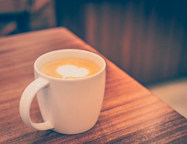 A cup of coffee with heart pattern in a white cup on wooden background.Vintage tone.