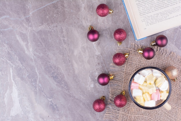 A cup of coffee with marshmallows and christmas balls around.