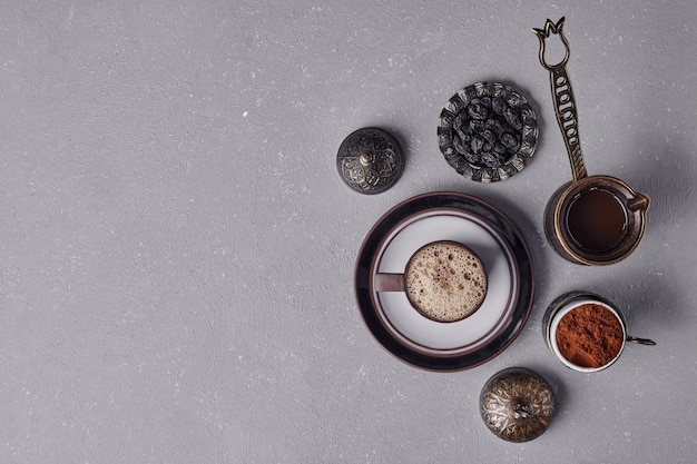 A cup of coffee with metallic pot and cinnamon powder around.