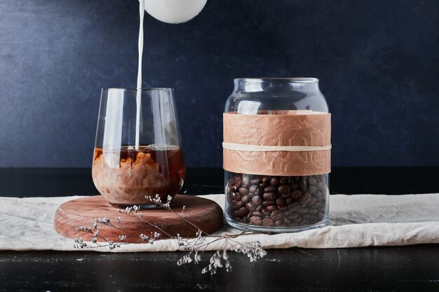 A cup of coffee with milk on a wooden board with beans in the jar.