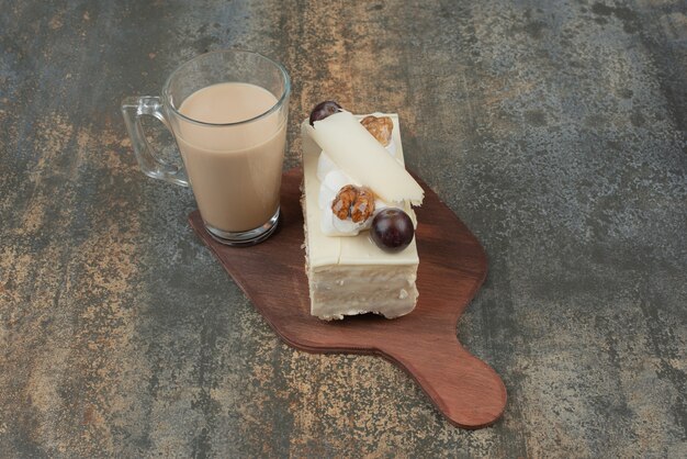 A cup of coffee with piece of cake on wooden board . 