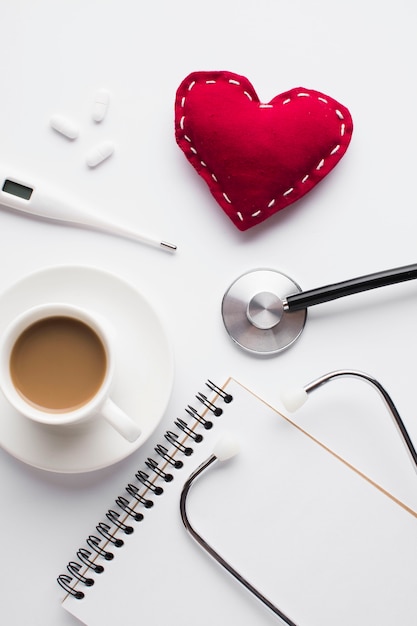 Cup of coffee with red toy heart and medical accessories over desk