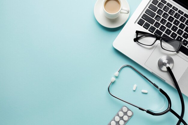 Cup of coffee with stethoscope on clipboard and pills over desk