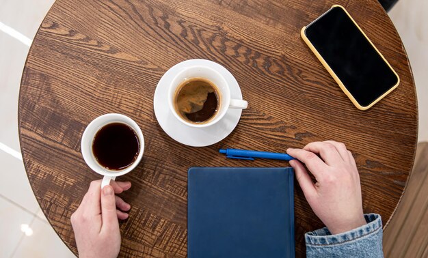 A cup of coffee on a wooden table and a notepad top view