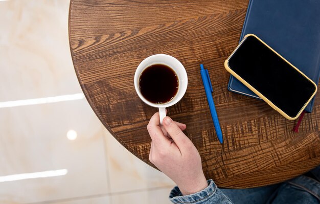 A cup of coffee on a wooden table and a notepad top view