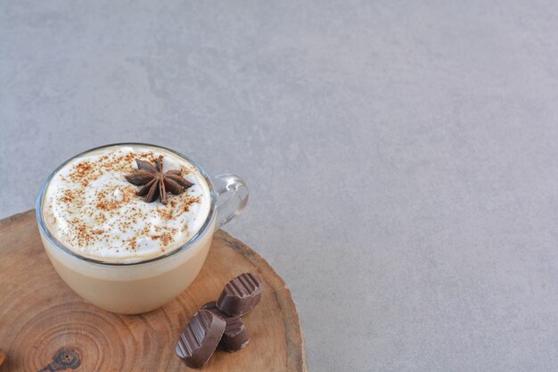 A cup of creamy coffee and cinnamon sticks on wood board.