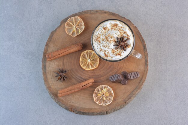 A cup of creamy coffee and cinnamon sticks on wood board.