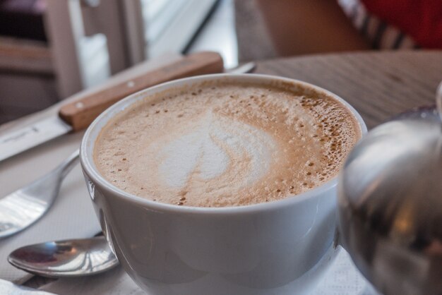 Cup of creamy coffee next to cutlery