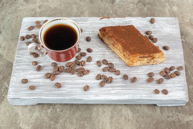 Cup of dark coffee with beans and pastry on wooden board