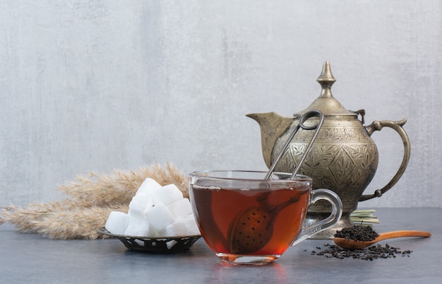 A cup of delicious tea with ancient kettle and sugar .