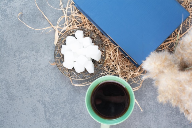 A cup of delicious tea with book and sugar on hay