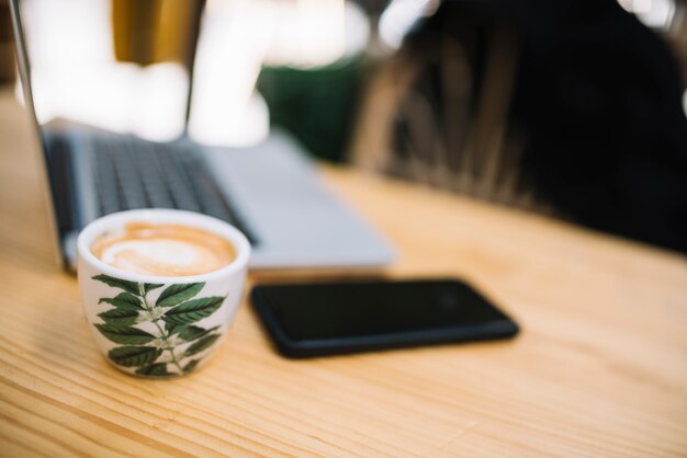 Чашка напитка возле мобильного телефона и ноутбука за столом в уличном кафе