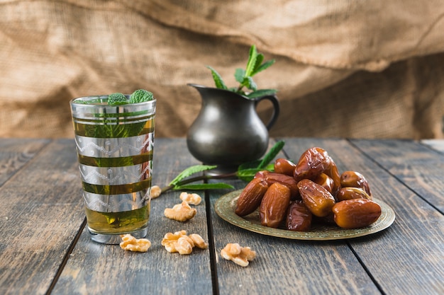Cup of drink near pitcher, nuts, plant twigs and dried fruits on table