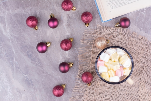 A cup of drink with marshmallows and red christmas balls around