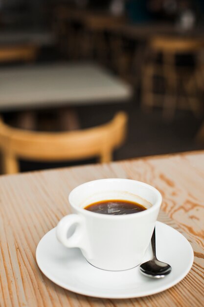 Cup of espresso coffee with stainless steel spoon over desk