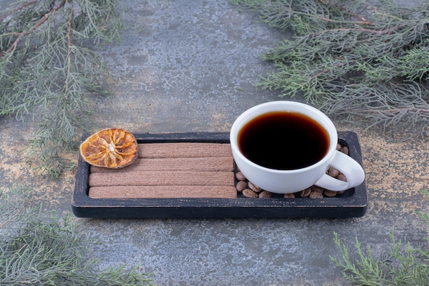 Cup of espresso, stick biscuits and coffee beans on black plate.