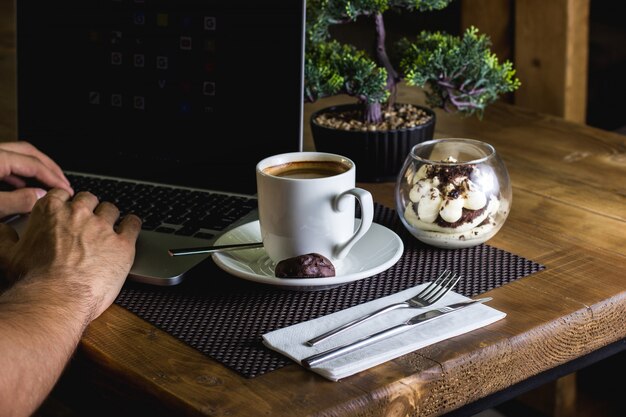 Free photo a cup of espresso and tiramisu served for man working in his notebook