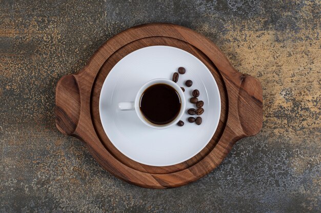 Free photo cup of espresso with coffee beans on wooden board.