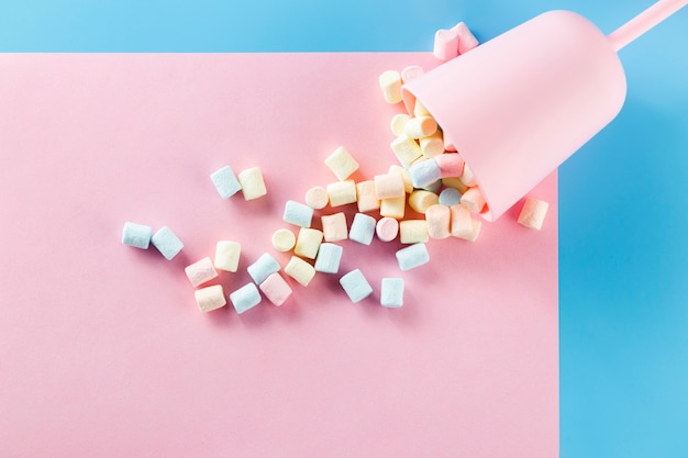 Cup filled with marshmallows on pink paper surface