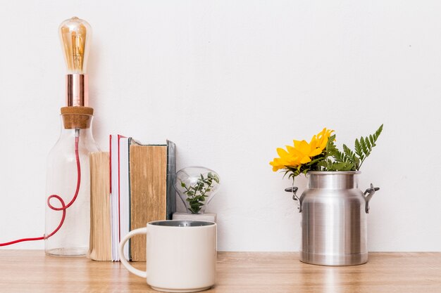 Cup flowers in tin can books and lamp on table