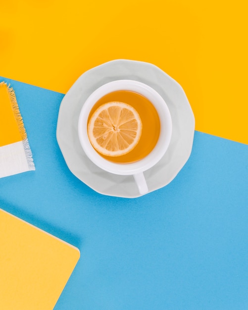 Cup of ginger tea with lemon on yellow and blue background