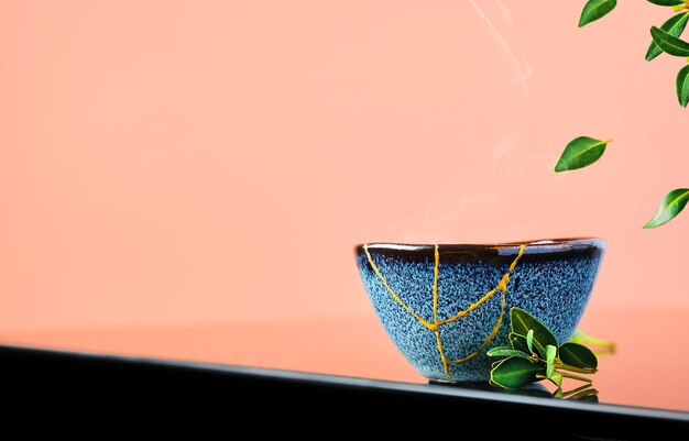 Cup of green Japanese tea , tea leaves fly over the cup. Selective focus on the cup. Steam rises above the bowl. Reclaimed ceramic blue cup, second life of things, recycling or kintsugi