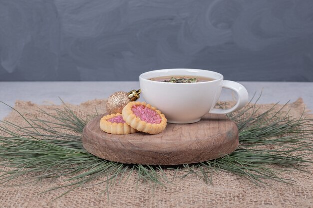 Cup of herbal tea, Christmas ball and cookies on wooden plate. 