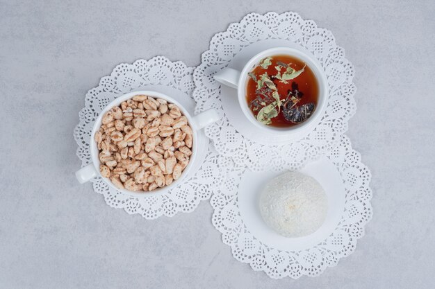 Cup of herbal tea, coconut cookie and bowl of sweets on white table. High quality photo