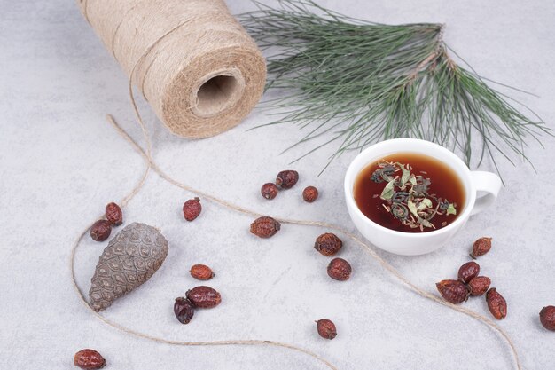 Cup of herbal tea, dried cranberries and pinecone on marble table. High quality photo