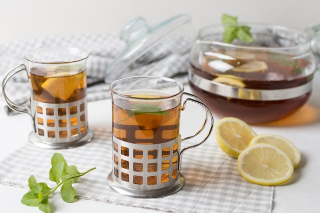 Free photo a cup of herbal tea glasses with lemon slices and mint on tablecloth