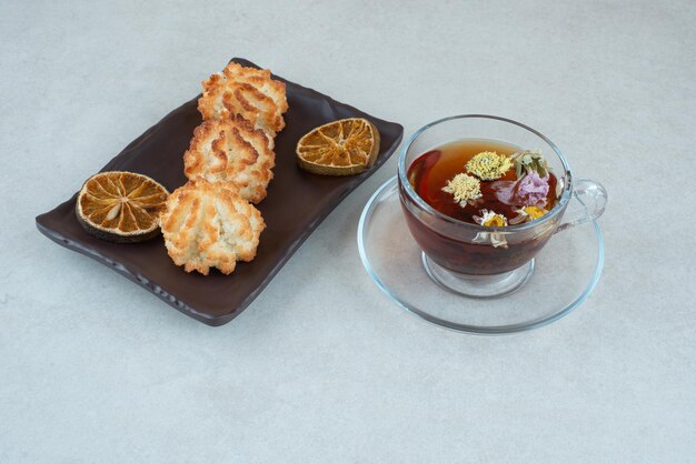 A cup of herbal tea with cookies and dried oranges on black plate.