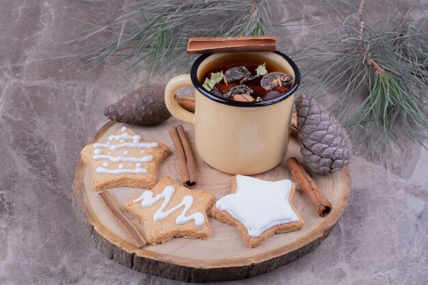 A cup of herbal tea with gingerbreads on a wooden board