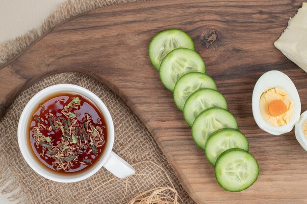 A cup of herbal tea with sliced cucumber and boiled egg .