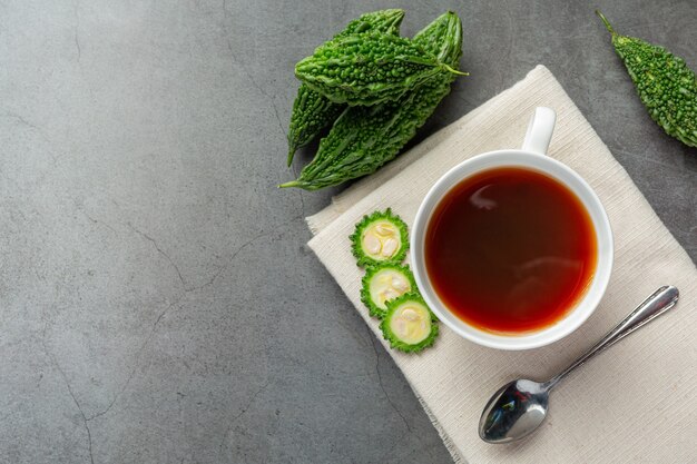 a cup of hot bitter gourd tea with raw sliced bitter gourd place on white fabric