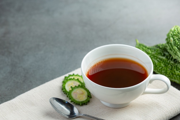 a cup of hot bitter gourd tea with raw sliced bitter gourd place on white fabric