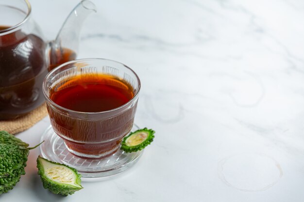 a cup of hot bitter gourd tea with raw sliced bitter gourd on white marble floor